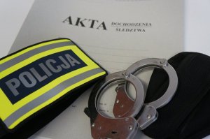 zdjęcie teczki akt na której lezy opaska identyfikująca policję oraz kajdanki