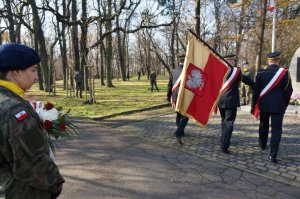 Na zdjęciu widac poczet sztandarowy składający się z trzech strażników miejsckich który zatrzymują się przed omnikiem Powstanców Śląskich. Po lewej stronie widać dziewczynę w mundurze będąca uczennicą klasy mundurowej