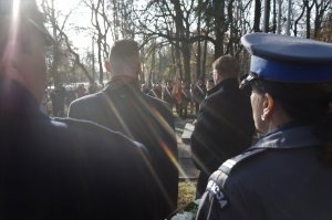 Zdjęcie zrobione zza pleców, przedstawia zbliżenie na strój wyjściowy szefowej świętochłowickich policjantów oraz Komedanta Strazy Miejsckiej. Przed nimi widac włodarzy miasta witających uczestników obchodów