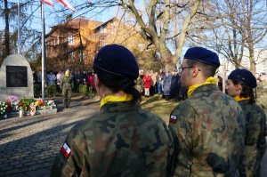 Zdjęcie wykonane za pleców umundurowanych uczniów klasy mundurowej, w tle widać pomnik Powstańców Śląskich oraz uczestników obchodów w tym przedstawicieli służb mundurowych