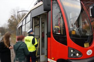 Na zdjęciu umundurowany policjant wraz z pracownicami sanepidu przed wejściem do tramwaju w celu przeprowadzenia kontroli stosowania się do obostrzeń