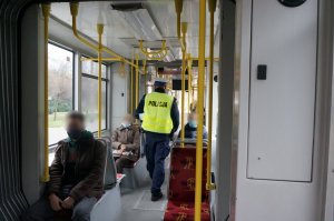 Na zdjęciu widać policjanta wewnątrz tramwaju w trakcie prowadzenia kontroli stosowania się do obostrzeń przed podróżnych