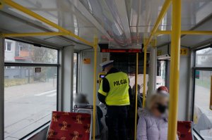 Na zdjęciu widać policjanta wewnątrz tramwaju w trakcie prowadzenia kontroli stosowania się do obostrzeń przed podróżnych