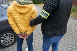 Nieumundurowany policjant prowadzi do budynku świętochłowickiej komendy zatrzymanego mężczyznę zakutego w kajdanki na ręce trzymane z tyłu