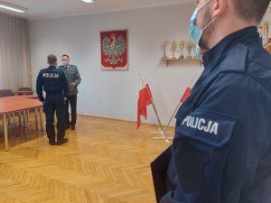 Uroczystość ślubowania w świętochłowickiej komendzie. Na zdjęciu widać Komendanta Miejskiego Policji w Świętochłowicach ktory wręcza dokument ślubowania nowo przyjętemu policjantowi. W tle widać pozostałych przyjętych policjantów