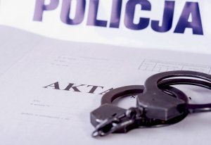 Na zdjęciu taśma z napisme policja. Przed nią widać teczkę akt dochodzenia/śledztwa oraz kajdanki