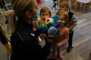 Na zdjęciu mundurowa z założoną na ręku pacynką imitującą maskotkę śląskiej Policji psa Sznupka w trakcie zabawy z przedszkolakami