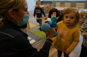 Na zdjęciu mundurowa z założoną na ręku pacynką imitującą maskotkę śląskiej Policji psa Sznupka w trakcie zabawy z przedszkolakami