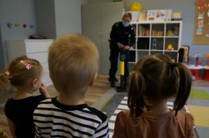Na zdjeciu policjantka w trakcie tłumczenia dzieciom zasad przechodzenia przez pasy oraz sygnalizacji świetlnej uprawniającej do przejścia przez jezdnię