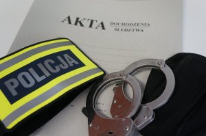 Na zdjeciu żółta opaska z napisem Policja, kajdanki oraz teczka akt dochodzenia/śledztwa