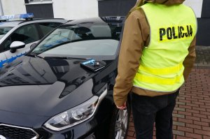 Na zdjęciu nieumundurowany policjant w kamizelce odblaskowej z napisem policja, za nim nowy nieoznakowany radiowóz