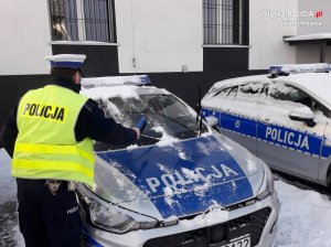 Na zdjęciu policjant w trakcie odśnieżania radiowozu