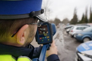 Na zdjęciu zbliżenie na policjanta drogówki który prowadzi pomiar prędkości przy pomocy ręcznego laserowego miernika.