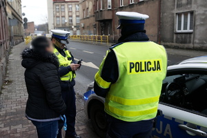 Na zdjęciu policjanci z drogówki w trakcie legitymowania kobiety, która popełniła wykroczenie polegające na przechodzeniu przez jezdnię w miejscu niedozwolonym.