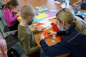 Na zdjęciu uczestnicy półkoloni wraz z mundurową przygotowują serca z wyznaniami dotyczącycmi bezpiecznych zachowań na drodze, które zostaną przekazane kierującym podczas Walentnkowych kontroli drogowych