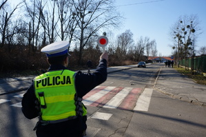 Na zdjęciu policjant z drogówki podczas zatrzymania do kontroli drogowej kierującego. Mindurowy ma uniesioną do góry ręke z tak zwanym lizakiem  za pomocą którego wskazuje kierującemu miejsce zatrzymania