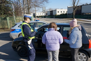 Na zdjęciu mundurowy wraz z dwoma dziewczynkami w trakcie przekazywania kierującemu serduszka z wyznaniem dotyczącymi bezpiecznych zachowań na drodze