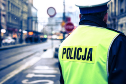 Na zdjęciu zbliżenie na napis Policja na żółtej odblaskowej kamizelce którą ma założoną policjant z drogówki, ktory prowadzi obserwację sytacji na drodze.