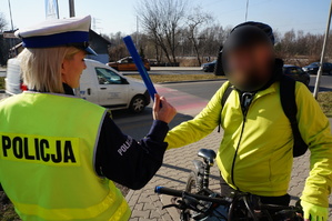 Na zdjęciu mundurowa przy jednym ze świętochłowickich przejść dla pieszych. Policjantka zakłada na rękę rowerzysty opaskę odblaskową.