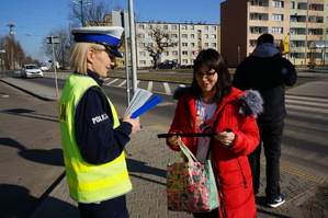 Na zdjęciu mundurowa przy jednym ze świętochłowickich przejść dla pieszych w towarzystwie pieszej, która trzyma w ręku opaskę odblaskową, otrzymaną od policjantki.