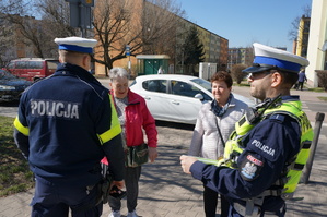 Na zdjęciu mundurowi podczas wręczania pieszym elementów odblaskowych w postaci opaski.