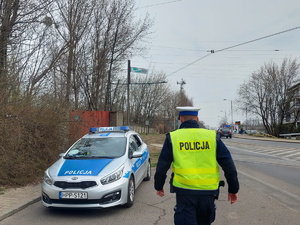 Na zdjęciu policjant z drogówki idzie w kierunku zaparkowanego radiowozu