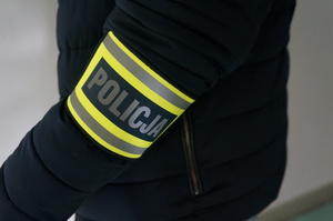 Na zdjęciu zbliżenie na opaskę odblaskową z napisem Policja na ramieniu nieumundurowanego policjanta