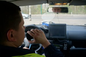 Na zdjęciu policjant drogówki wewnątrz radiowozu w trakcie zgłaszania dyżurnemu przebiegu kontroli dorgowej