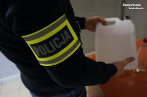 Na zdjęciu zbliżenie na butelkę z trunkiem niewiadomego pochodzenia, którą trzyma w rękach nieumundurowany policjant