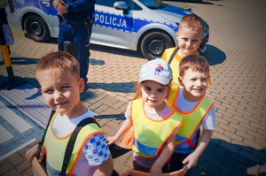 zbliżenie na dzieci które, biorą udział w zajęciach profilaktycznych. Dzieci mają założony jeden z elementów mini miasteczka ruchu drogowego, który przedstawia autobus.