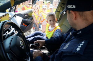 Na zdjęciu mundurowy oraz przedszkolak wewnątrz radiowozu. Policjant prezentuje dzieciom radiowóz policyjny