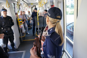 Wnętrze tramwaju, w ktorym widać mudnurowych oraz seniorów. Policjantka trzyma mikrofon w dłoni i prowadzi prelekcję dla uczestników akcji profilaktycznej
