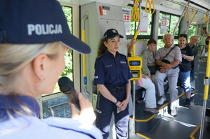 Wnętrze tramwaju, w ktorym widać dwie policjantki oraz seniorów. Policjantki prowadzą prelekcję dla uczestników akcji profilaktycznej. Jedna z mundurowych trrzyma mikrofon w dłoni