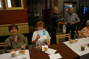 zdjęcie z wnętrza Muzeum Powstań Śląskich. Na zdjęciu widać seniorów siedzących przy stolikach oraz policjantkę która rozdaje im koperty życia