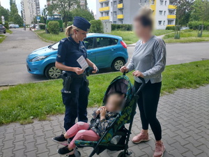 Policjantka umundurowana stoi przy kobiecie, która prowadzi wózek z dzieckiem