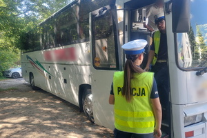 Na zdjęciu policjantka stojąca plecami do obiektywu. Przed nią stoi autokar, który kontroluje inny policjant