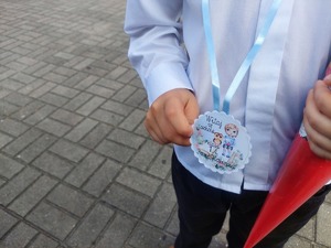 zbliżenie na zawieszkę trzymaną w dłoni dziecka z napisem Witaj w szkole klasa 1a pani Halinka.