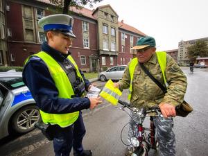 umundurowany policjant wręczający rowerzyście kamizelkę odblaskową