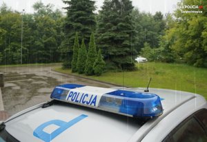 Na zdjęciu zbliżenie na napis policja znajdujący się na belce oświetleniowej na dachu radiowozu. W tle widać padający deszcz.