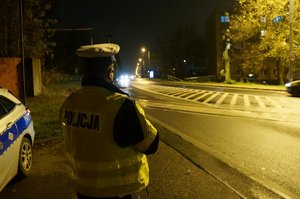 Na zdjęciu policjant z drogówki w trakcie obserwacji sytuacji na drodze po zmroku. Mundurowy zwraca uwagę na prawidłowe oświetlenie pojazdów.