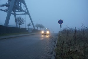 Na zdjęciu widać jadący, wyłaniąjący się zza gęstej mgłym radiowóz.