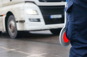 zdjęcie nogi policjanta z wiszącą przy niej tarczą do zatrzymywania pojazdów na tle samochodu ciężarowego