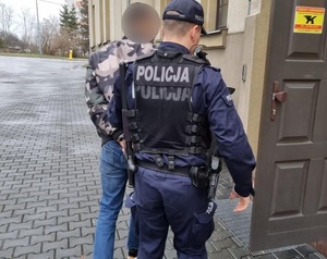 policjant prowadzi zatrzymanego do budynku