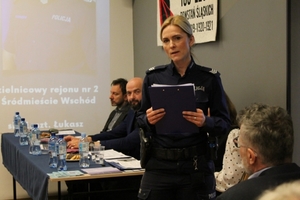 policjantka prowadząca debatę przemawia przy stole po prawej stronie ekranu