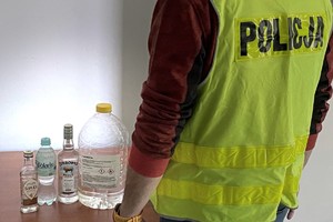 policjant stoi przy stole na którym znajduje się podrobiony alkohol w butelkach i bańce 5 litrowej