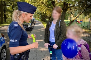 na zdjęciu policjantka wręcza gadżety dziewczynce na hulajnodze