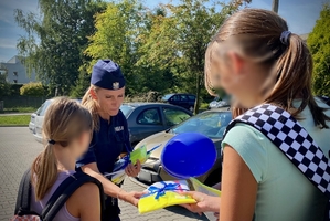 na zdjęciu policjantka wręcza upominki dzieciom pod szkołą