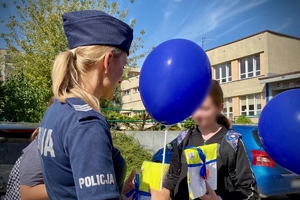 na zdjęciu policjantka wręcza upominki dzieciom pod szkołą