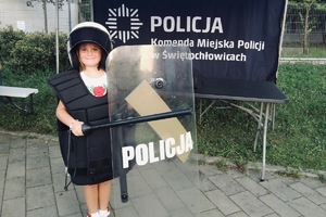 na zdjęciu dziewczynka w kamizelce i kasku, trzyma w rękach tarczę z napisem policja