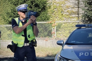 na zdjęciu policjant podczas pomiaru prędkości stoi obok radiowozu